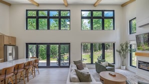 Ein großzügiger Wohnbereich mit einer großen Schiebeglasdoor zum Deck, einer Küche mit Kühlschrank und einem Kamin.