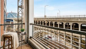 A balcony with a view of a bridge, a chair, and a small table with a plant and a mug. - Modern Flats Retreat  Free Parking & Gym (Cleveland)
