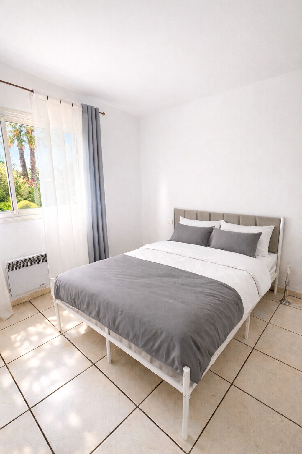 A bedroom with a bed, curtains, a window, and a radiator.