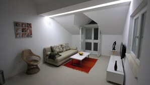 A living room with a sofa, a wicker chair, a coffee table, a TV, and a window with shutters. - Modern Flat With sea View (Orebic)