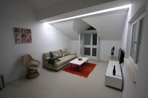 A living room with a sofa, a wicker chair, a coffee table, a TV, and a window with shutters. - Modern Flat With sea View (Orebic)
