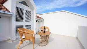 A balcony with wicker furniture, a bottle of wine, and a white building. - Modern Flat With sea View (Orebic)