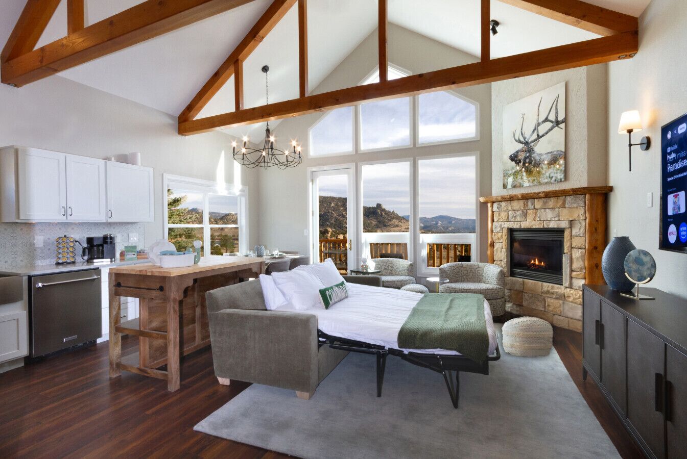 Amplia sala de estar con chimenea, comedor con cocina y ventanas grandes que ofrecen vistas del paisaje.