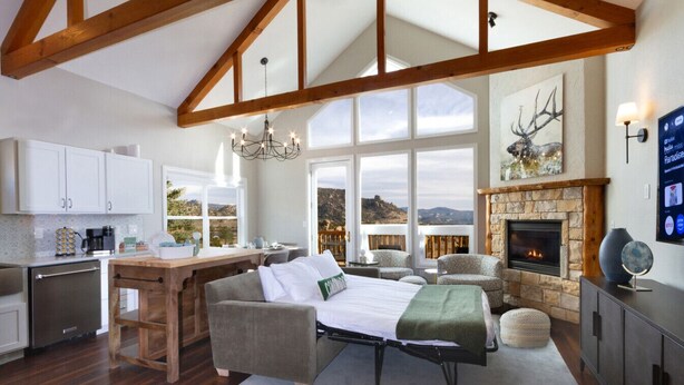 Amplia sala de estar con chimenea, comedor con cocina y ventanas grandes que ofrecen vistas del paisaje.