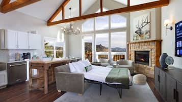 Amplia sala de estar con chimenea, comedor con cocina y ventanas grandes que ofrecen vistas del paisaje.