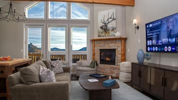Una sala de estar acogedora con chimenea de piedra, ventanas amplias, un televisor y vistas a las montañas.