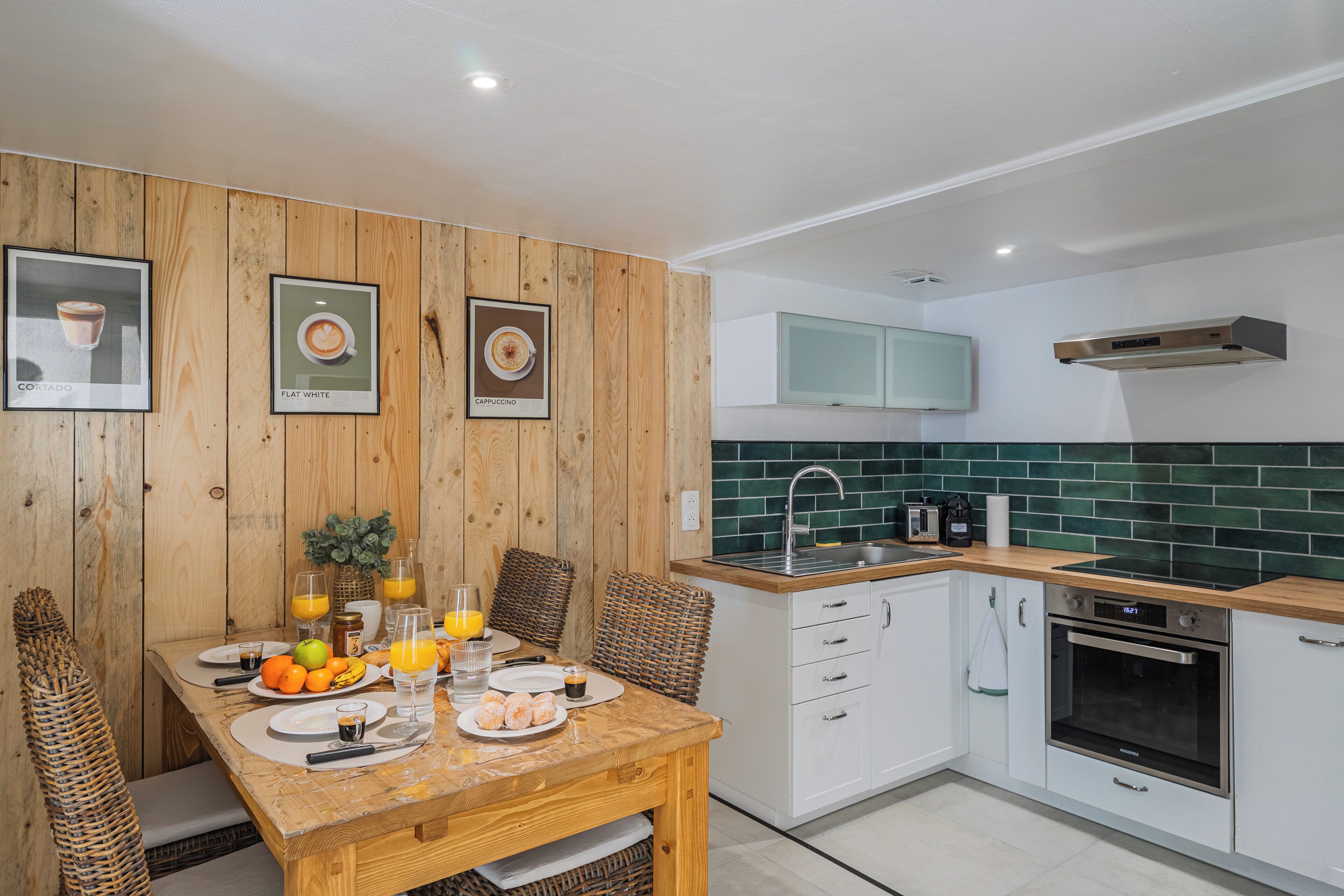 Een moderne keuken met een houten eettafel, witte kastjes en een groene achterwand.