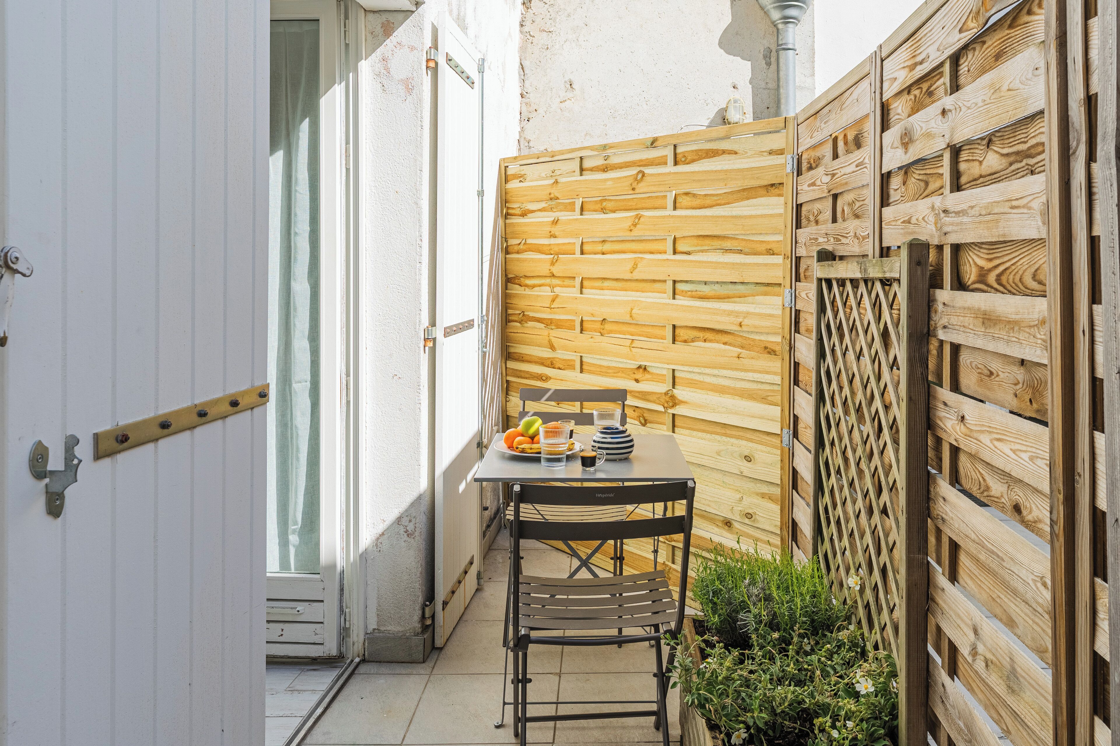 Eine kleine Terrasse mit Tisch und Stühlen, einem Holzzaun und einer Tür.