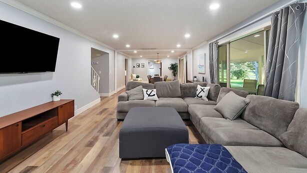 A modern living room with a sectional sofa, a flat-screen TV, wooden flooring, and large windows. - 5BR Boise Retreat | Perfect for Groups or Families (Boise)