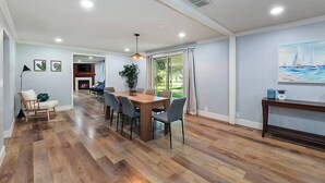 A spacious room with a wooden floor, a dining area with a table and chairs, a fireplace, and a large window with curtains. - 5BR Boise Retreat | Perfect for Groups or Families (Boise)