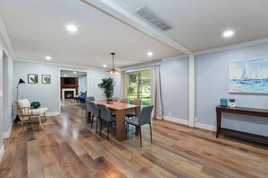 A spacious room with a wooden floor, a dining area with a table and chairs, a fireplace, and a large window with curtains. - 5BR Boise Retreat | Perfect for Groups or Families (Boise)