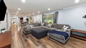 A modern living room with a sectional sofa, ottoman, and a flat-screen TV. - 5BR Boise Retreat | Perfect for Groups or Families (Boise)
