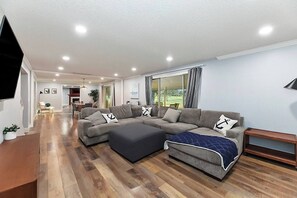 A modern living room with a sectional sofa, ottoman, and a flat-screen TV. - 5BR Boise Retreat | Perfect for Groups or Families (Boise)