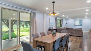 A modern living room with a wooden dining table, grey upholstered chairs, a grey sofa, and a large window with a view of a green lawn. - 5BR Boise Retreat | Perfect for Groups or Families (Boise)