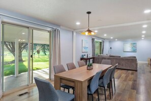 A modern living room with a wooden dining table, grey upholstered chairs, a grey sofa, and a large window with a view of a green lawn. - 5BR Boise Retreat | Perfect for Groups or Families (Boise)