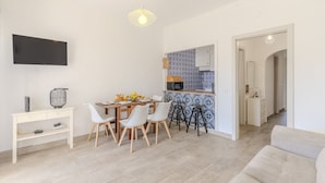 A modern kitchen with a tiled backsplash, a dining area with a table and chairs, a flat-screen TV mounted on the wall, and a light fixture above the dining table. - #374 Cozy & Bright Stay | City Comfort (Albufeira)