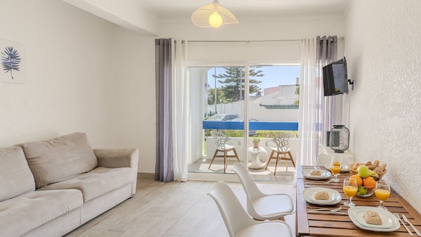A modern living room with a sofa, dining table, chairs, and a TV. - #374 Cozy & Bright Stay | City Comfort (Albufeira)