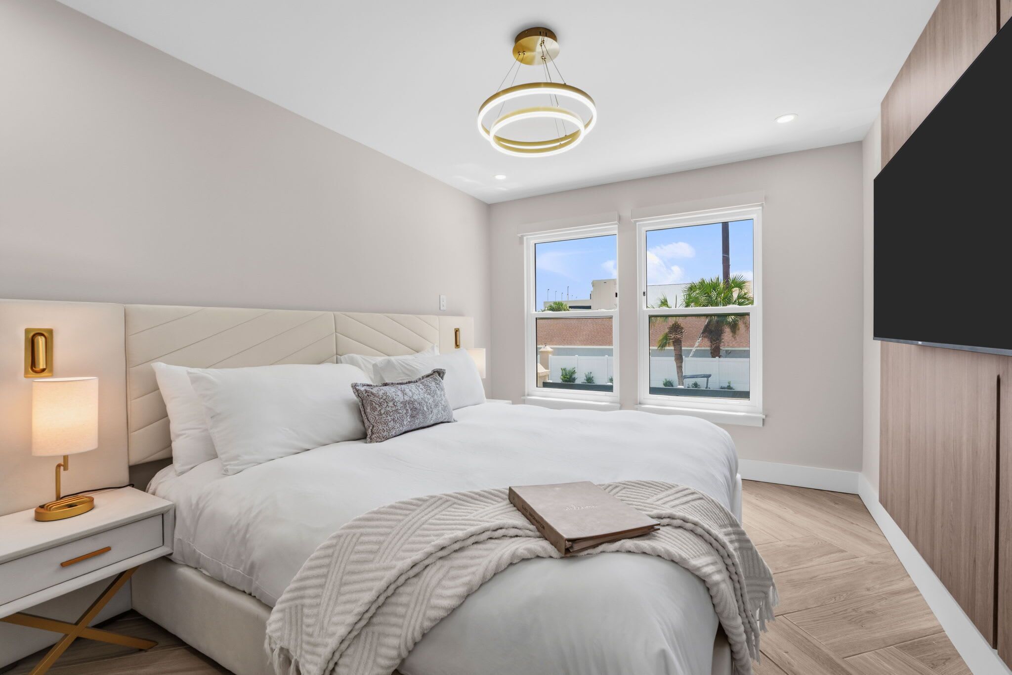 A modern bedroom with a bed, bedside table, lamp, and a large window.