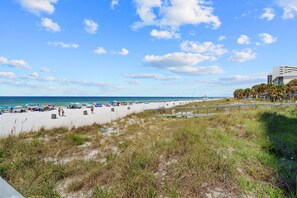 Ein Strand mit Promenadenweg, Strandsonnenschirmen und einem Pier in der Ferne.