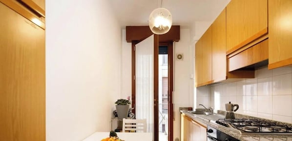 Une cuisine avec des meubles en bois, une cuisinière à gaz, un évier et un luminaire suspendu.