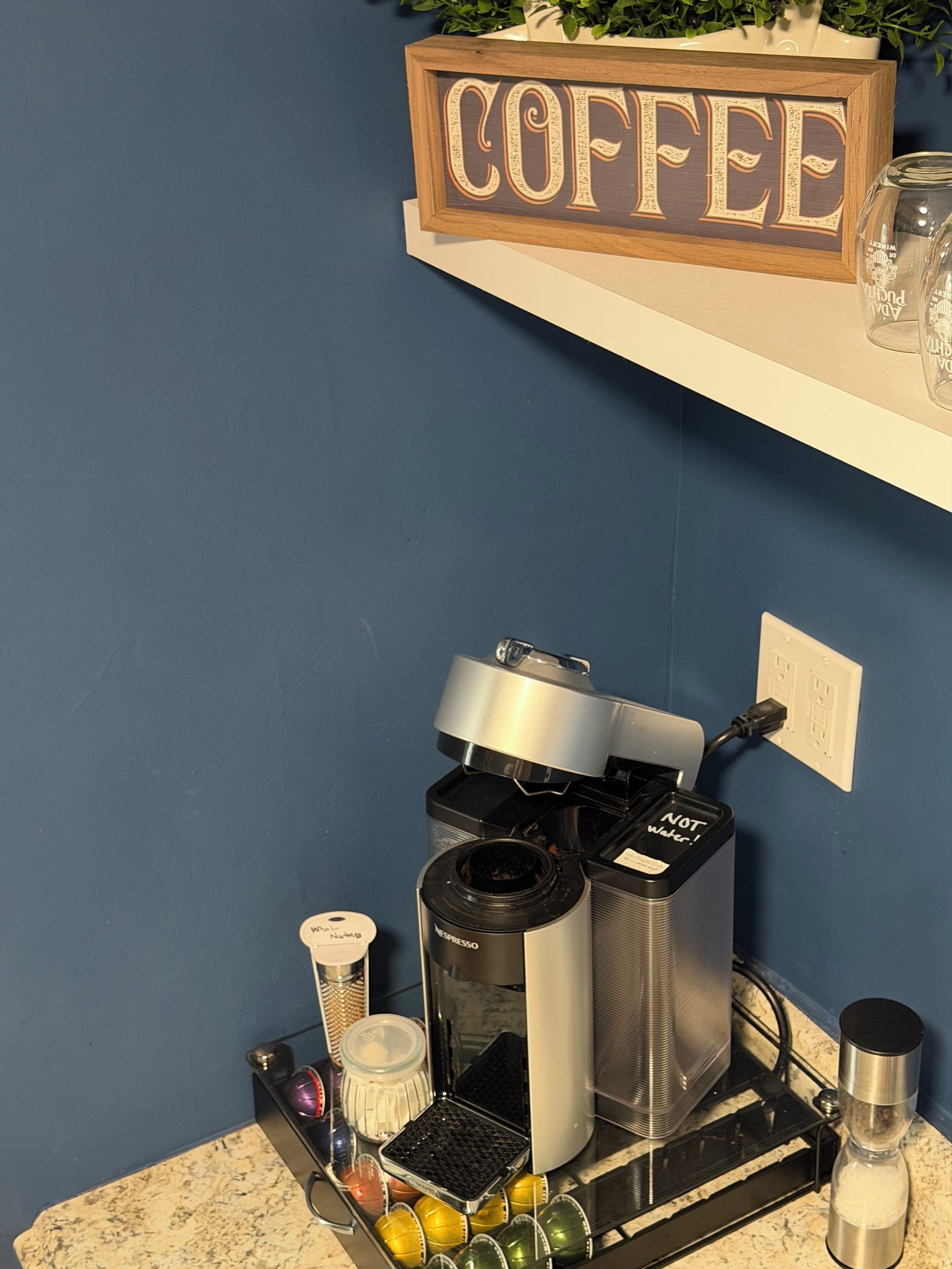 A coffee maker on a countertop with a coffee sign above it.