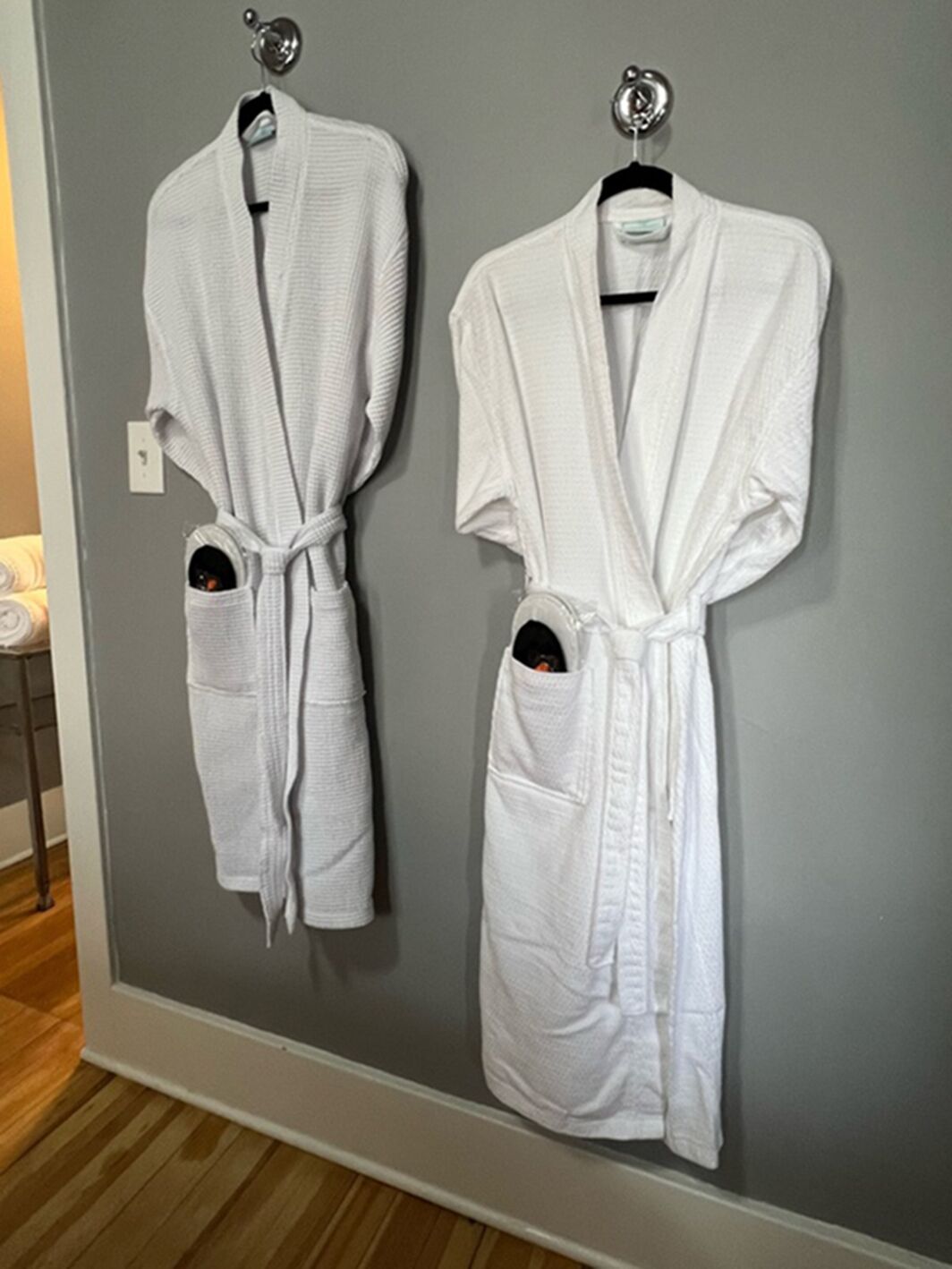 Two white bathrobes hanging on a wall.