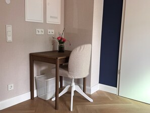 A small office space with a wooden desk, a white chair, a vase with flowers, and a blue door. - Design Apartment Limburg an der Lahn- HAHLGARTEN SUITES (Limburg an der Lahn)