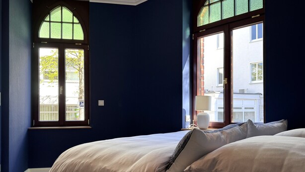 Un dormitorio con cama, mesita de noche, lámpara y ventana con vistas al exterior.