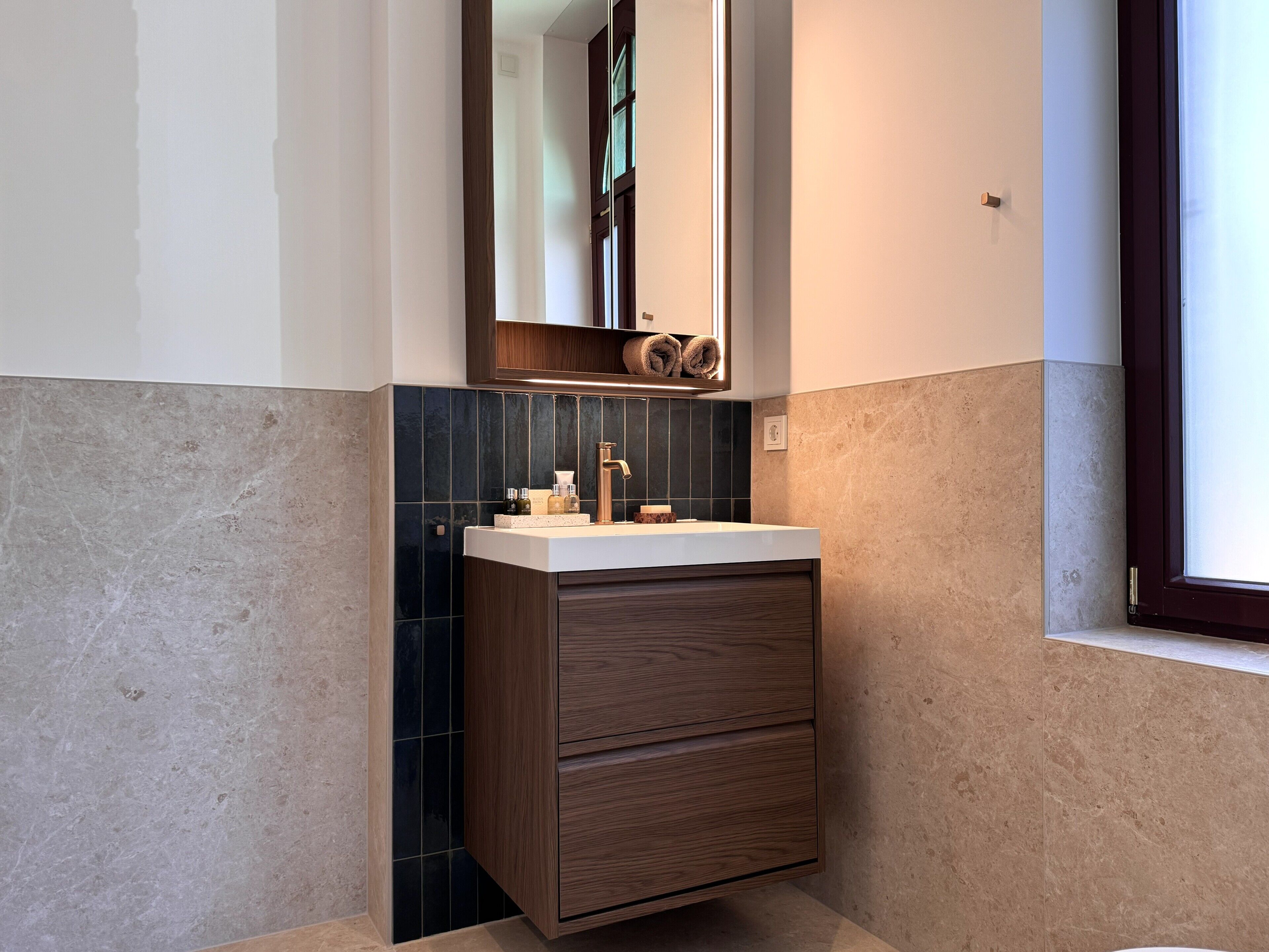Une salle de bain moderne avec un meuble-lavabo, des carreaux foncés et un meuble en bois.