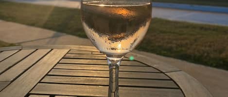 A glass of water on a wooden table with a sunset in the background.