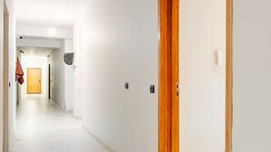 Un corridoio con una porta in legno, un tappetino d'ingresso, un interruttore della luce e un telefono fissato alla parete.