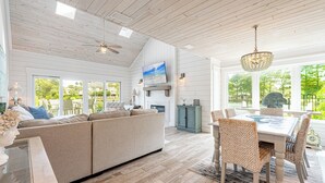 A spacious living room with a large sofa, dining table, and chairs, a fireplace, and a view of the outdoors. - Lakefront Luxury • Golf Cart Included (Miramar Beach)