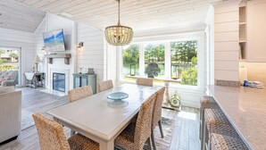 A spacious dining area with a large table and wicker chairs, a television mounted on the wall, and a view of a lake through large windows. - Lakefront Luxury • Golf Cart Included (Miramar Beach)