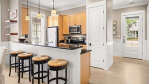 A modern kitchen with a central island, wooden cabinets, a microwave, and a refrigerator. There are three stools with woven seats. - Private beach cottage + golf cart (Miramar Beach)