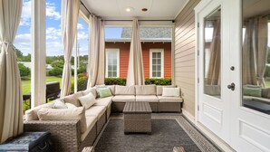 A covered porch with a sectional sofa, a small table, and a door leading to a house. - Private beach cottage + golf cart (Miramar Beach)