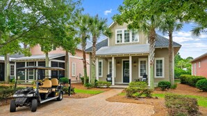 A two-story house with a covered porch, a golf cart, and a well-maintained garden. - Private beach cottage + golf cart (Miramar Beach)