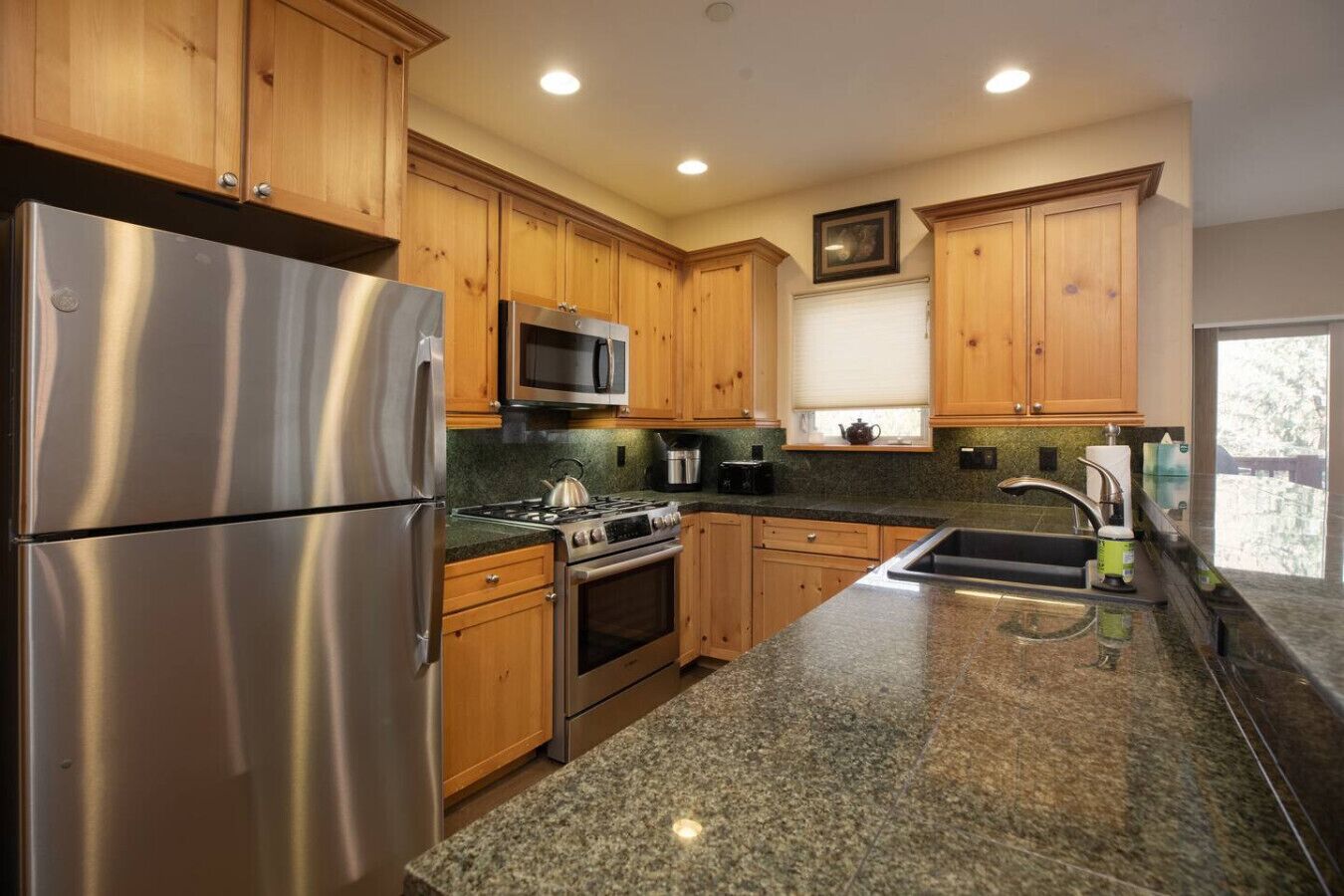 Una cocina moderna con armarios de madera, electrodomésticos de acero inoxidable, encimeras de granito y una ventana con persianas.