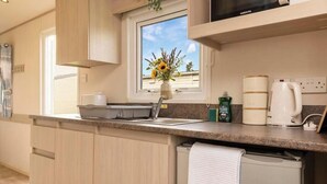 Una cocina moderna con armarios de madera, un microondas integrado, un lavamanos y un ventanal con vista al cielo.
