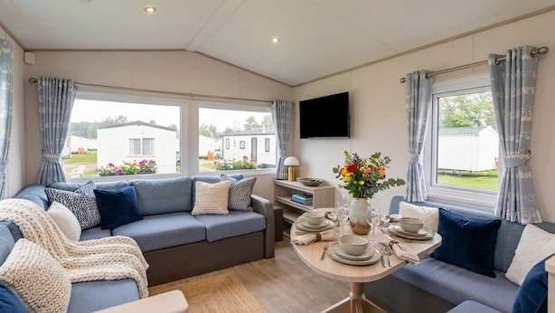 Una sala acogedora con un conjunto de sofás, una mesa de comedor para cuatro personas y ventanas amplias con vistas al exterior.