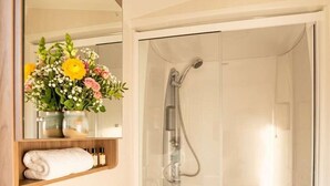 Een badkamer met een wit wastafelmeubel, een douchecabine van glas en een spiegel met een bloemenvaas.