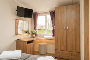 A bedroom with a bed, a desk, a TV, a window with curtains, and a wardrobe.