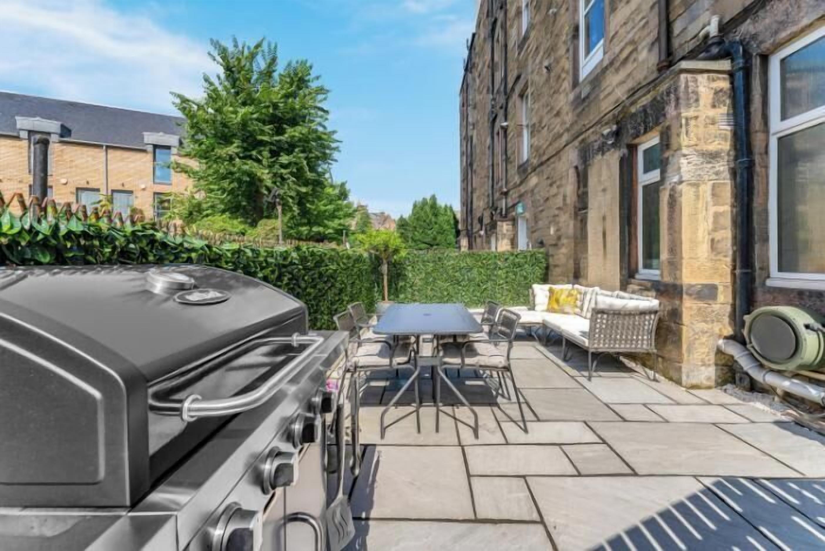 Une terrasse avec un barbecue, des sièges d’extérieur et une haie.