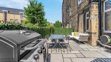Une terrasse avec un barbecue, des sièges d’extérieur et une haie.