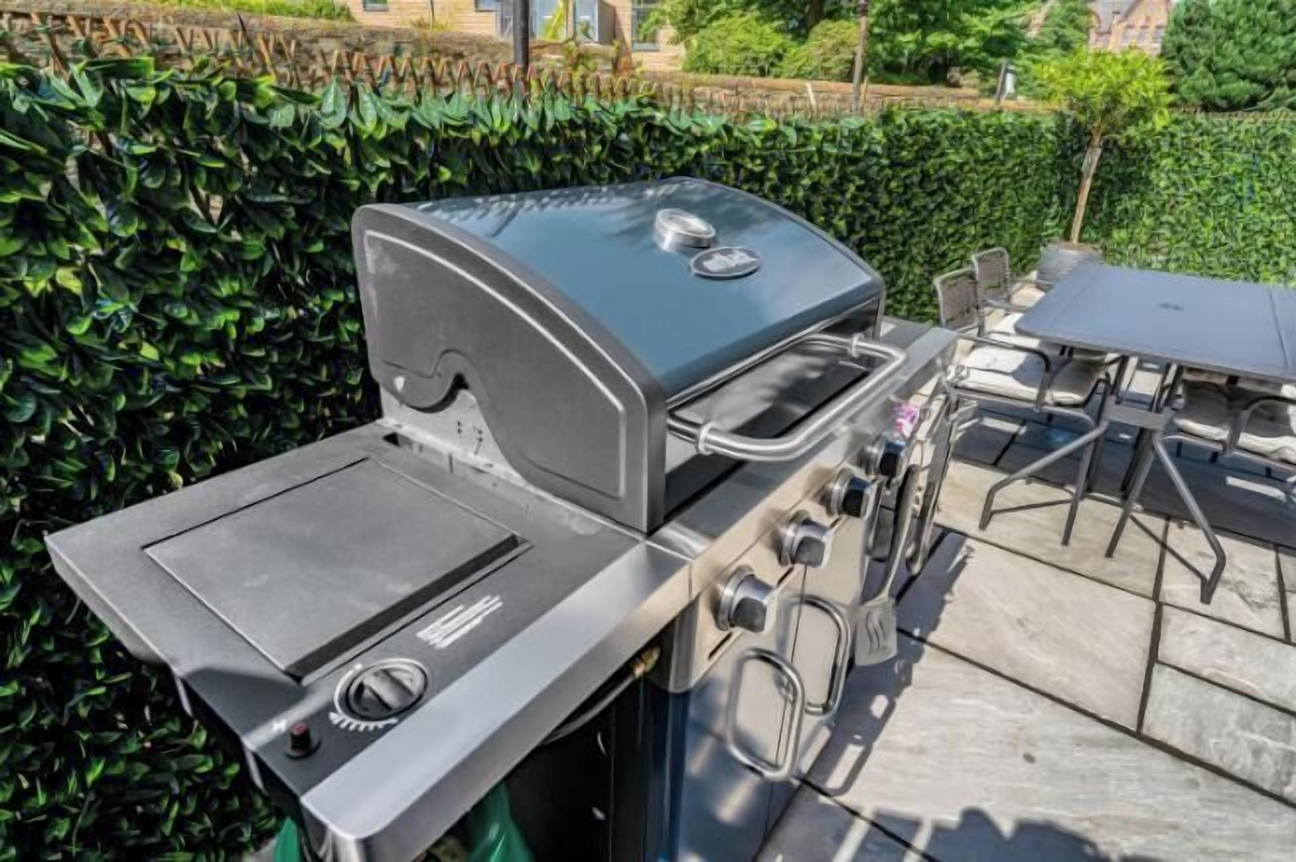 A stainless steel grill with a lid, a side burner, and a flat cooking surface.