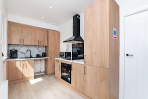 A modern kitchen with wooden cabinets, a black range hood, and a built-in oven. - Free Parking & WiFi Near St Andrews, Leven Beach (Methil)