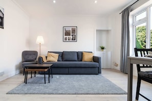 A modern living room with a grey sofa, a small table, a lamp, and a framed picture on the wall. - Free Parking & WiFi Near St Andrews, Leven Beach (Methil)