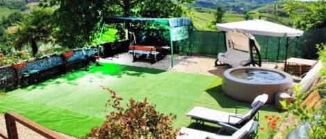 A backyard with a hot tub, a covered seating area, and a lawn.