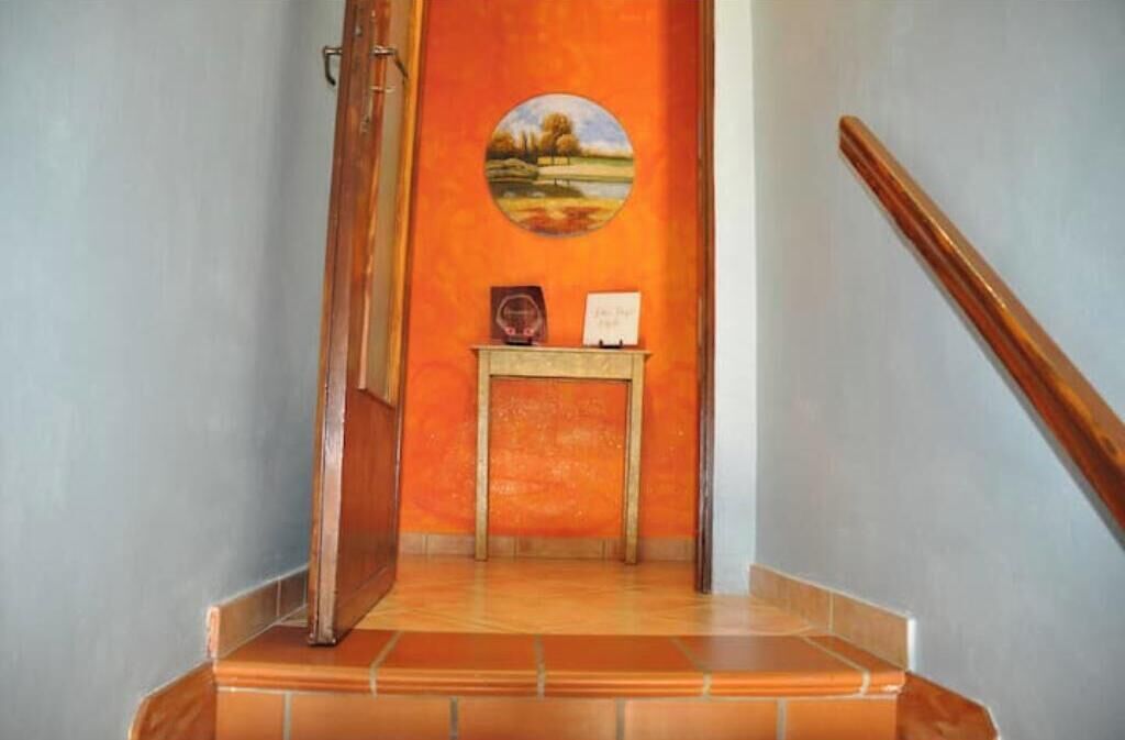 A staircase with a wooden handrail, a small table with a framed picture and a plaque, and a wall with a circular painting.