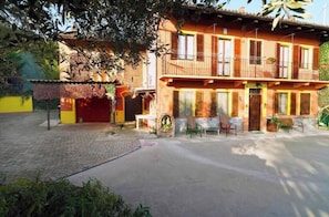 A two-story building with a balcony, a paved courtyard, and a small garden area. - Il Casale del Roero - Relaxation among Vineyards, Nature and Tradition (Canale)