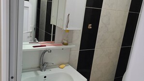A bathroom with a white sink, mirror, and cabinet, a toilet, and black and white tiled walls. - Room-standard Twin Bedroom (Istanbul)